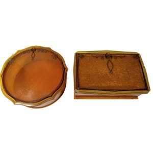 May include: A round amber-coloured glass container with a scalloped edge and a rectangular amber-coloured glass box with a gold-toned metal frame. Both items feature a delicate black line-art floral design on the lid surfaces.