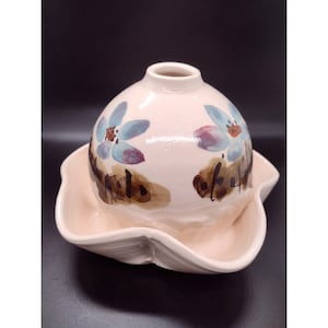 Könnte beinhalten: Eine rosafarbene Keramikvase mit rundem Korpus und einem breiten, gewellten Sockel. Die Vase ist mit blauen Blumen und braunen Pinselstrichen verziert.