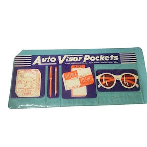 May include: A vintage blue car visor organiser with compartments. It features a Camel cigarette advert, two pens, a Kleenex box, and sunglasses. The text "Auto Visor Pockets" is printed across the top.