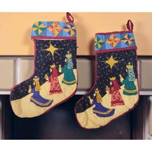 May include: Two Christmas stockings with a dark blue background adorned with a star and figures of the Three Wise Men. The stockings have a yellow base, red trim, and a patchwork cuff with blue, yellow, and red geometric patterns.