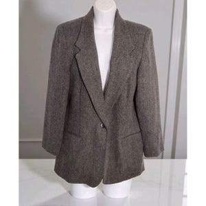 May include: A brown blazer with a single-button closure, displayed on a white mannequin. The blazer has a notched lapel, two front pockets, and three-quarter sleeves. The fabric appears to be a textured wool blend.