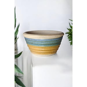 May include: A ceramic bowl with a light brown glaze and blue and green stripes. The bowl is round and has a wide rim.