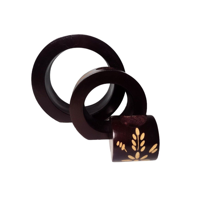 Peut inclure: Une sculpture en bois brun fonc&eacute; compos&eacute;e de trois anneaux imbriqu&eacute;s. La sculpture pr&eacute;sente un motif floral peint en or sur l'anneau inf&eacute;rieur.