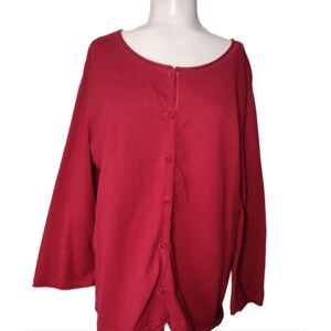 May include: A long-sleeved, button-up cardigan in a deep red color. The cardigan has a simple, classic design with a round neckline.