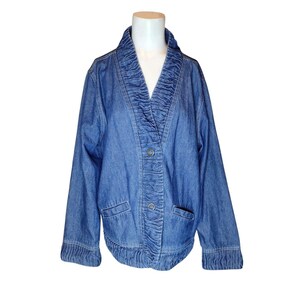 May include: A blue denim jacket with a ruffled collar and button closure. The jacket has two pockets on the front and a gathered waist.