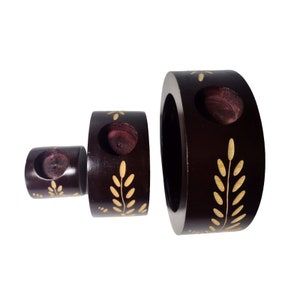 Peut inclure: Ensemble de trois bougeoirs en bois brun avec des motifs en feuilles d'or. Les bougeoirs sont ronds et ont un trou au centre pour une bougie. Le plus grand bougeoir mesure environ 20 cm de diam&egrave;tre.