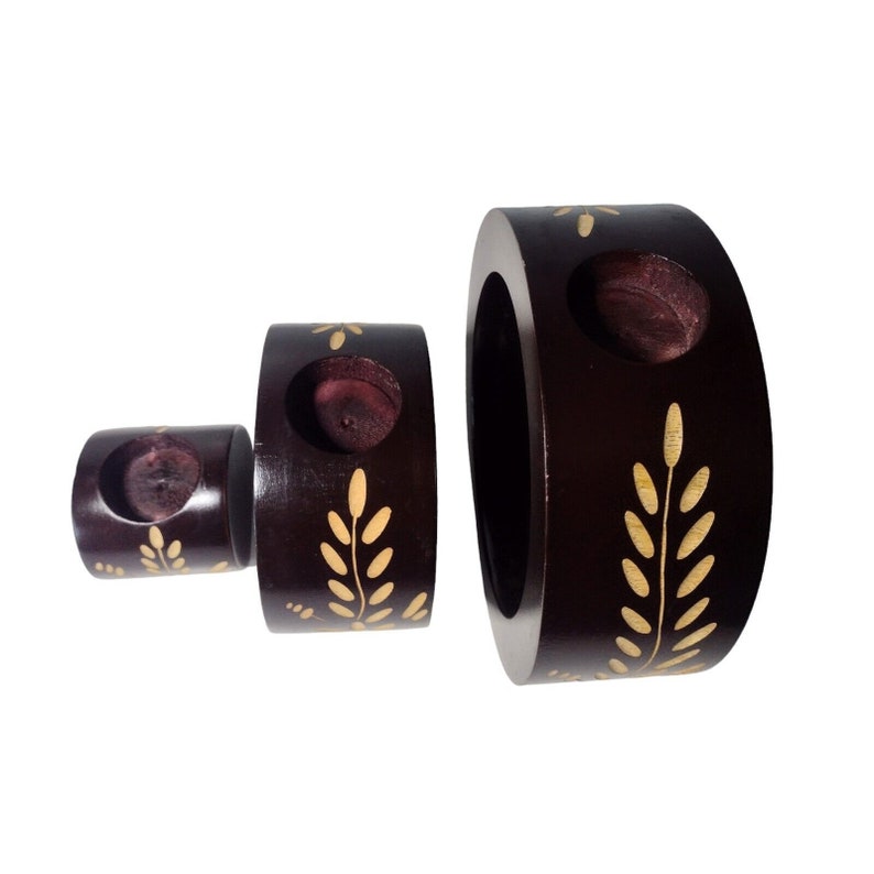 Peut inclure: Ensemble de trois bougeoirs en bois brun avec des motifs en feuilles d'or. Les bougeoirs sont ronds et ont un trou au centre pour une bougie. Le plus grand bougeoir mesure environ 20 cm de diam&egrave;tre.