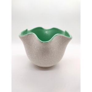 May include: A ceramic bowl with a ruffled rim. The exterior is a speckled, light gray, while the interior and rim are a vibrant green. The bowl has a unique, organic shape, perfect for serving or display.