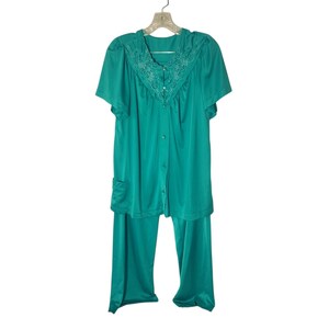 May include: Teal-colored pajama set with a button-down top and matching pants. The top features short sleeves, a decorative embroidered collar, and a small pocket. The set is hanging on a clear plastic hanger.