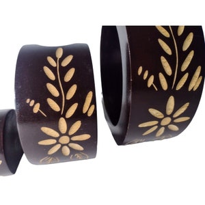 Peut inclure: Ensemble de quatre anneaux de serviette en bois brun avec un motif floral sculpt&eacute;. Les anneaux ont un motif floral brun clair sculpt&eacute; dans le bois brun fonc&eacute;.