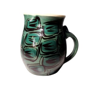 May include: A green ceramic mug with a black geometric pattern. The mug has a rounded body and a handle.