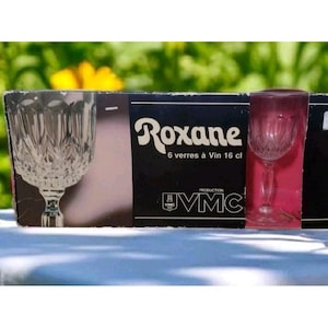 Puede incluir: Una caja de seis copas de vino Roxane, cada una con una capacidad de 16 cl. Las copas son transparentes con un diseño decorativo. La caja es negra con texto blanco y un logotipo.