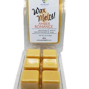 May include: Six amber wax melts in a clear plastic container. The label reads "Wax Melts! Amber Romance" with the brand name "Jane Bernard Aromatics".