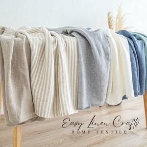 May include: A collection of different linen fabrics in various colors and patterns, including solid beige, striped beige, gray, white, blue, and green. The fabrics are draped over a wooden table with the text "Easy Linen Crafts HOME TEXTILE" printed below.