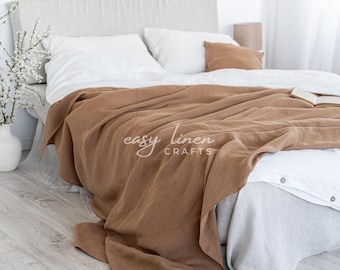 Può includere: Una coperta di lino marrone drappeggiata su un letto bianco con cuscini di lino bianco. La coperta ha il testo "easy linen crafts" stampato su di essa.