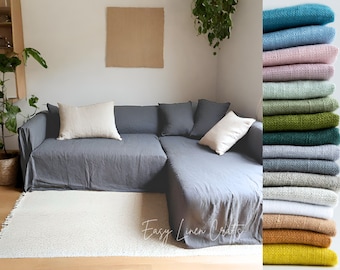 Puede incluir: Un sofá de lino gris con dos almohadas de lino blanco y una manta de lino blanca. El sofá está en una sala de estar con una alfombra blanca y un marco de imagen marrón en la pared. La imagen también muestra una pila de muestras de tela de lino en varios colores, incluyendo turquesa, azul claro, rosa, verde y blanco.
