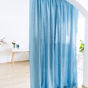 May include: A light blue linen curtain hangs from a wooden rod in a white room. The curtain is gathered at the top and falls in soft folds. The bottom of the curtain is on the floor. The text "Easy Linen Crafts" is visible in the lower right corner of the image.