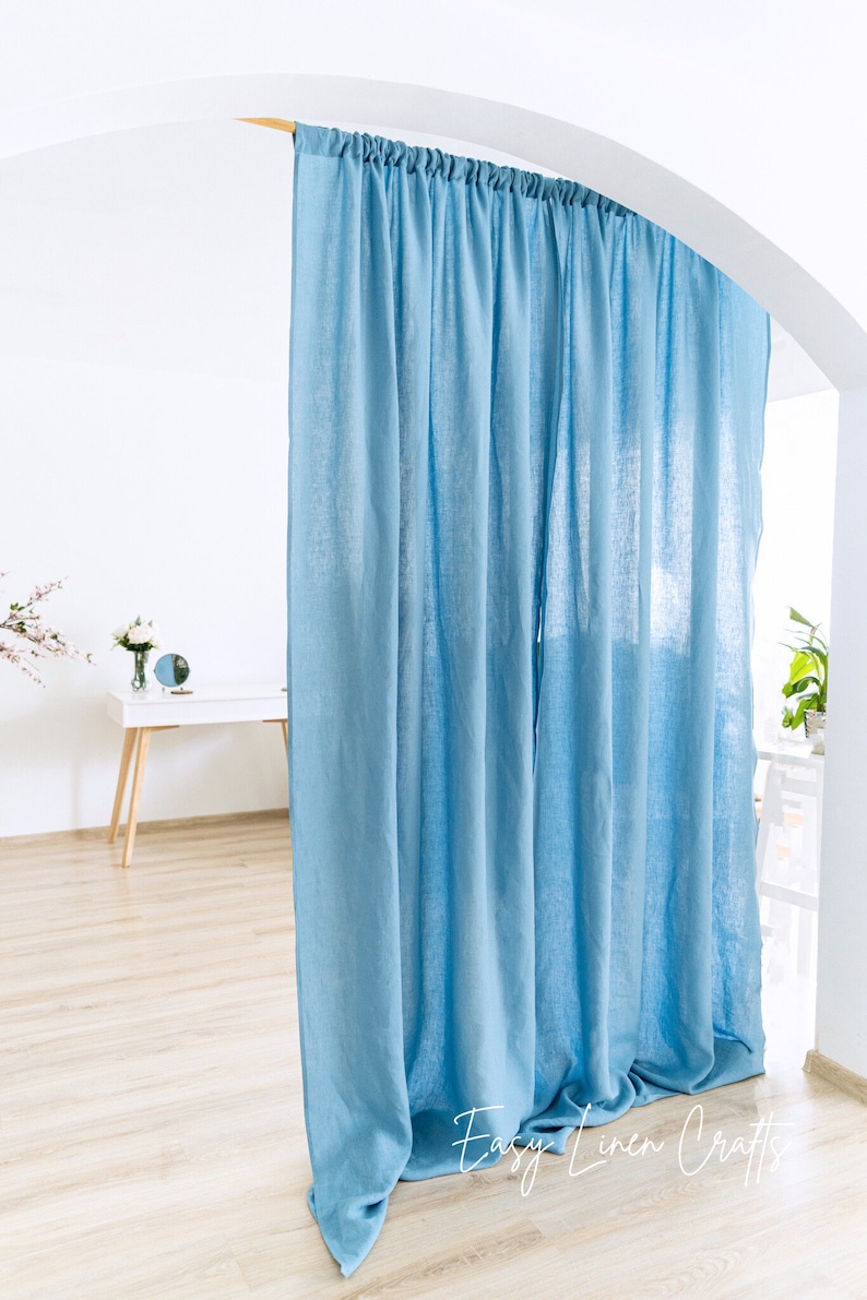 May include: A light blue linen curtain hangs from a wooden rod in a white room. The curtain is gathered at the top and falls in soft folds. The bottom of the curtain is on the floor. The text "Easy Linen Crafts" is visible in the lower right corner of the image.