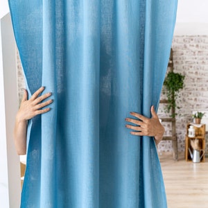 May include: A light blue linen curtain with a subtle texture. The curtain is hanging in a room with a wooden floor and a brick wall in the background.