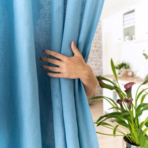 May include: A hand pulls back a light blue linen curtain, revealing a room with a plant in a silver pot. The text "Easy Linen Crafts" is visible in the bottom left corner of the image.