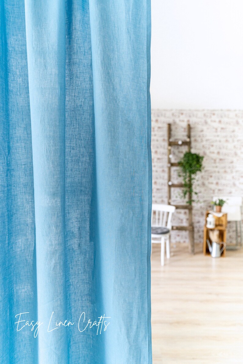 May include: A light blue linen curtain hangs in a room with a wooden ladder and a brick wall in the background. The text "Easy Linen Crafts" is visible at the bottom of the image.