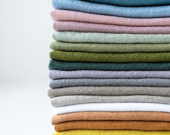 May include: A vertical stack of folded square fabric napkins in a variety of colors including teal, light blue, dusty pink, sage green, olive, dark green, lavender, gray, white, tan, orange, and yellow, all featuring a visible woven texture.