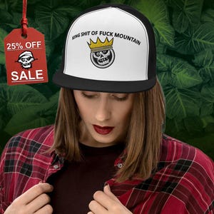 Könnte beinhalten: Eine schwarz-weiße Trucker-Kappe mit einem weißen Frontpanel. Das Frontpanel zeigt einen Schädel mit einer goldenen Krone und dem Text "King Shit of Fuck Mountain".
