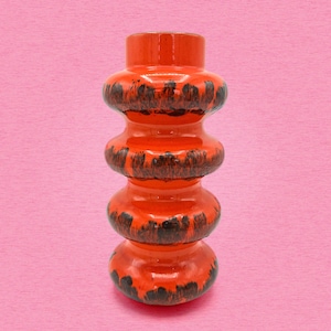 May include: A cylindrical ceramic vase featuring a vibrant orange glossy glaze with dark brown drip-like accents. The vase has a stacked, segmented design consisting of four rounded, bulbous tiers that create a distinct, undulating vertical profile.