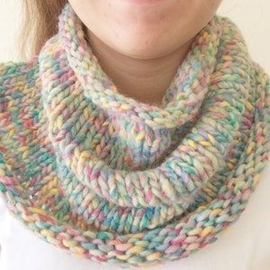 May include: A chunky knit infinity scarf featuring a variegated yarn pattern with blended pastel colors including pink, yellow, blue, and green. The scarf is constructed with a thick, textured rib stitch that creates a voluminous, circular loop design.