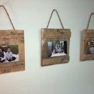 May include: Three rustic wooden picture frames with rope hangers and metal clips. Each frame holds a different photograph.