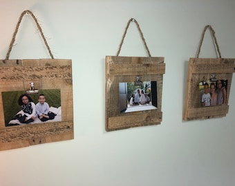 May include: Three rustic wooden picture frames with rope hangers and metal clips. Each frame holds a different photograph.