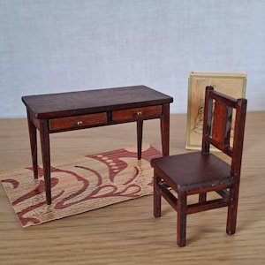 Könnte beinhalten: Miniatur-Holzschreibtisch mit zwei Schubladen, passendem Stuhl und kleinem Teppich mit rotem und cremefarbenem Muster. Der Schreibtisch und der Stuhl sind dunkelbraun. Ein kleines Buch ist sichtbar.