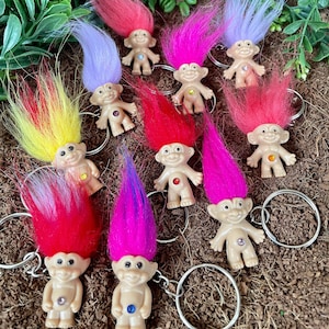 May include: A set of nine colorful troll keychain charms with jeweled belly buttons. Each troll has a different colored hair and a different colored jewel.