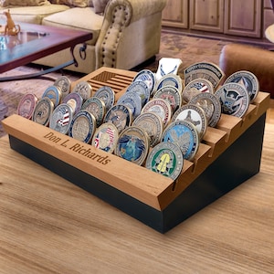 May include: A wooden challenge coin display case with multiple coins. The case has a black base and a light wood top with slots to hold the coins. The top is engraved with the American flag and the name "Don L. Richards".