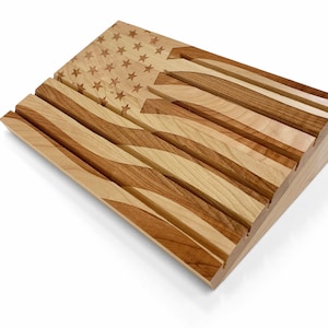May include: A wooden American flag, crafted from light and dark wood. The flag features stars and stripes, with a three-dimensional design. The stars are carved into the upper left corner, and the stripes are carved in a wave pattern.