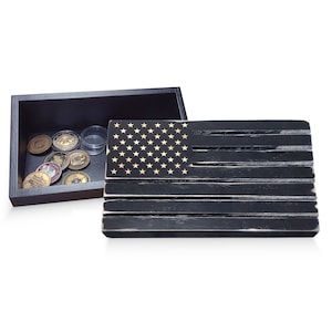 May include: A black wooden American flag with gold stars and stripes, next to a dark wooden box containing coins and clear containers. The flag has a distressed finish, and the box is open.