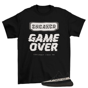 May include: Black t-shirt with a pixelated graphic that says "SNEAKER GAME OVER CONTINUE? [YES] NO" and a pair of black and white sneakers with the text "SPLY-350" on the side.