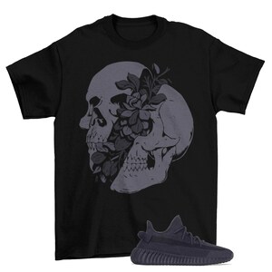 May include: Black t-shirt with a graphic of a skull with flowers growing out of its eye socket. A pair of dark grey Yeezy sneakers are shown in the bottom right corner of the image.