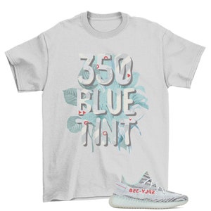 May include: A light gray t-shirt with the text "350 BLUE TINT" in a floral design. A pair of blue and white striped sneakers with red accents is in the lower right corner.