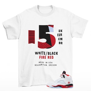 May include: White t-shirt featuring a large "15" graphic in black and red, with the text "WHITE/BLACK FIRE RED MADE IN USA BEAVERTON, OREGON." A white and red sneaker is at the bottom. The shirt also has the text "UK EUR CM BR."