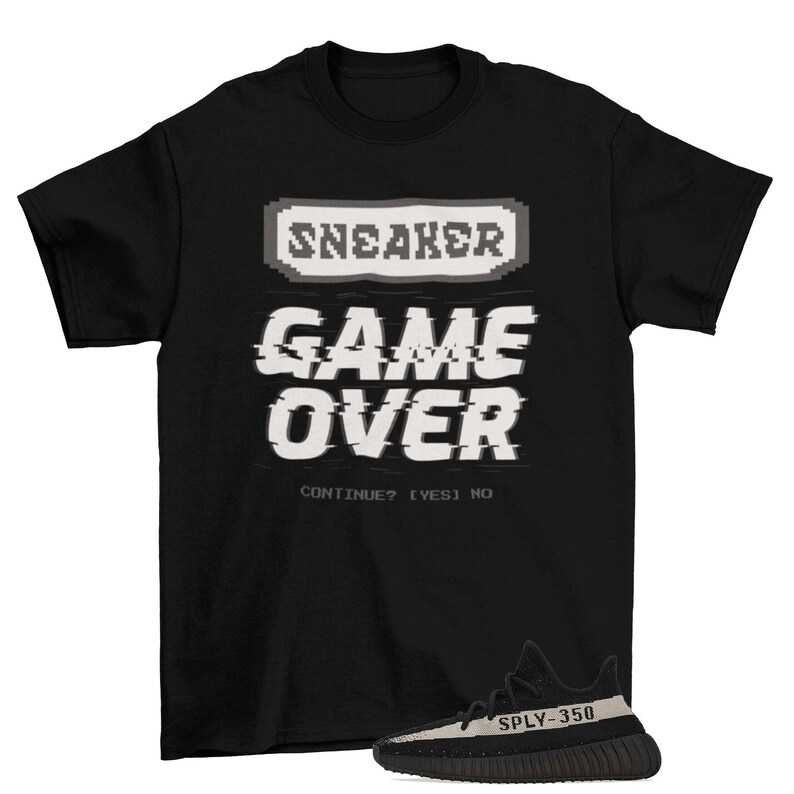 May include: Black t-shirt with a pixelated graphic that says "SNEAKER GAME OVER CONTINUE? [YES] NO" and a pair of black and white sneakers with the text "SPLY-350" on the side.