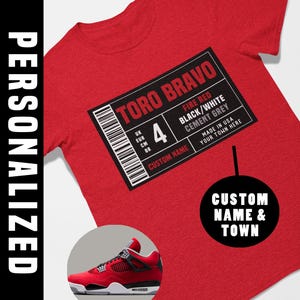 May include: Red t-shirt with a graphic label that reads "TORO BRAVO" and "FIRE RED BLACK/WHITE CEMENT GREY". The shirt features a sneaker graphic and the text "CUSTOM NAME & TOWN".