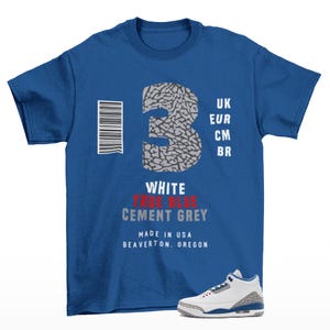 May include: A royal blue short-sleeve t-shirt featuring a large grey elephant-print number 3, a barcode, and text including UK, EUR, CM, BR, WHITE, TRUE BLUE, CEMENT GREY, MADE IN USA, BEAVERTON, OREGON, with a white, blue, and grey sneaker graphic.