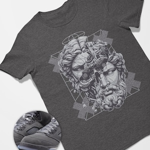 May include: Dark gray t-shirt featuring a detailed graphic of a classical bust merged with robotic elements. The design is in shades of gray and white. A pair of gray sneakers with gray laces and a translucent sole are in the lower left corner.
