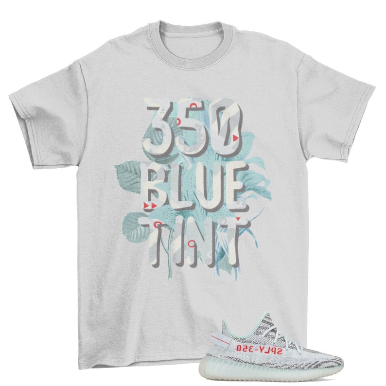 May include: A light gray t-shirt with the text "350 BLUE TINT" in a floral design. A pair of blue and white striped sneakers with red accents is in the lower right corner.