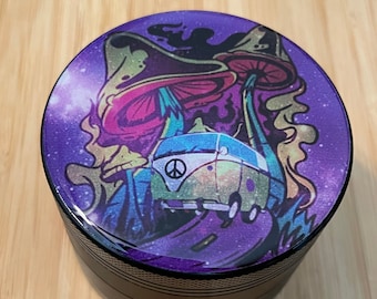 May include: A black metal grinder with a purple, green, and blue psychedelic design featuring a mushroom and a van with a peace sign.