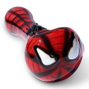 May include: A red and black glass smoking pipe with a Spiderman design. The pipe features a white spider web pattern and a white spider design on the side.