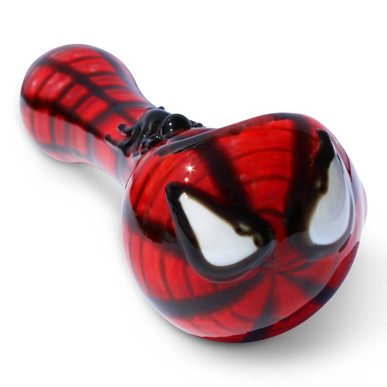 May include: A red and black glass smoking pipe with a Spider-Man design. The pipe is shaped like a traditional spoon pipe with a bowl and a mouthpiece.