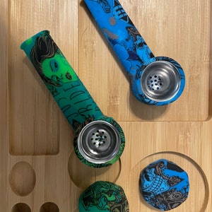 May include: Two silicone smoking pipes with colourful skull and floral designs. The pipes have a metal bowl with holes for airflow.