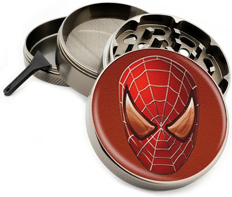 May include: A silver metal grinder with a red and black Spider-Man design on the lid. The grinder has a screen, a compartment for collecting kief, and a scraper.